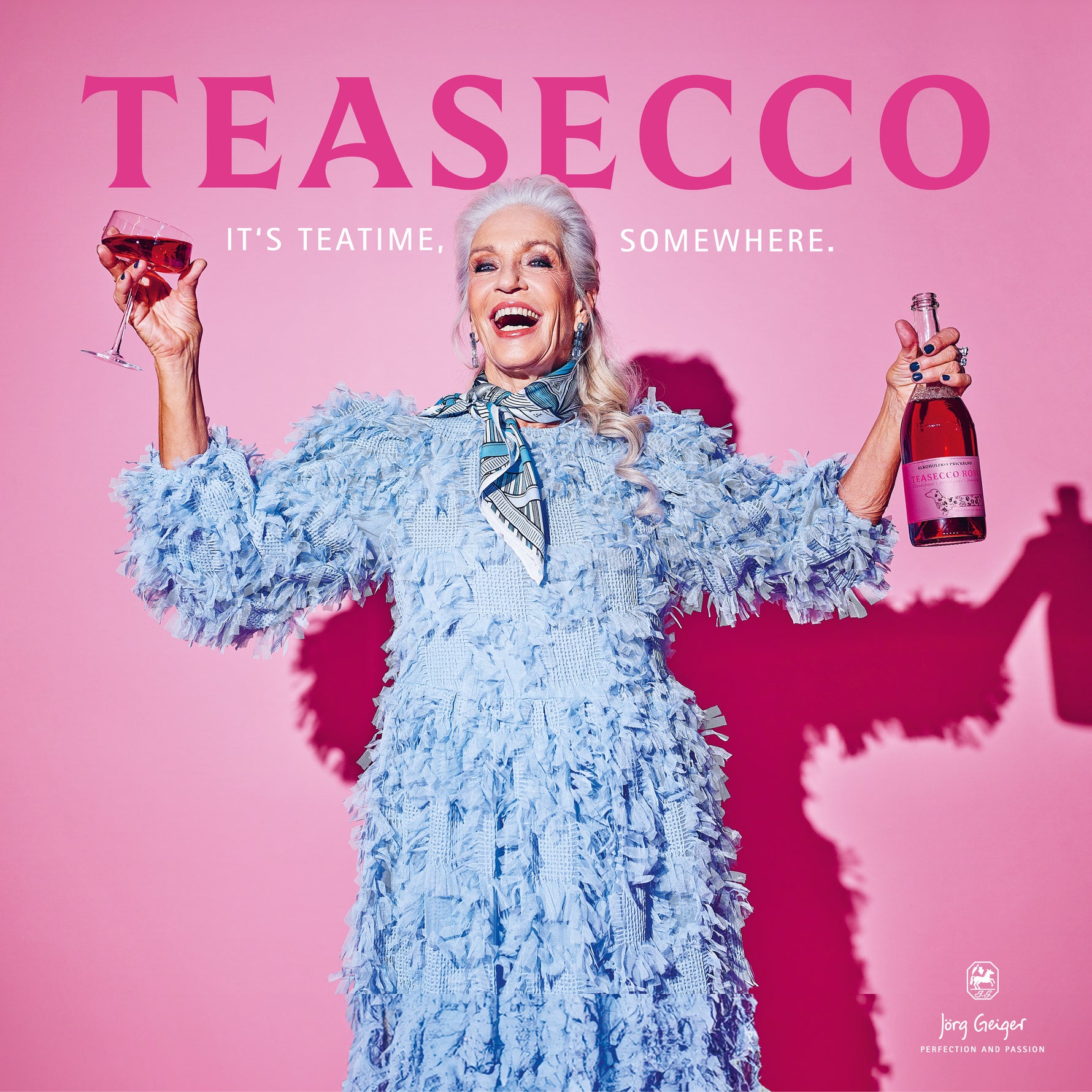 Woman in a blue dress holding a glass and bottle of Teasecco against a pink background
